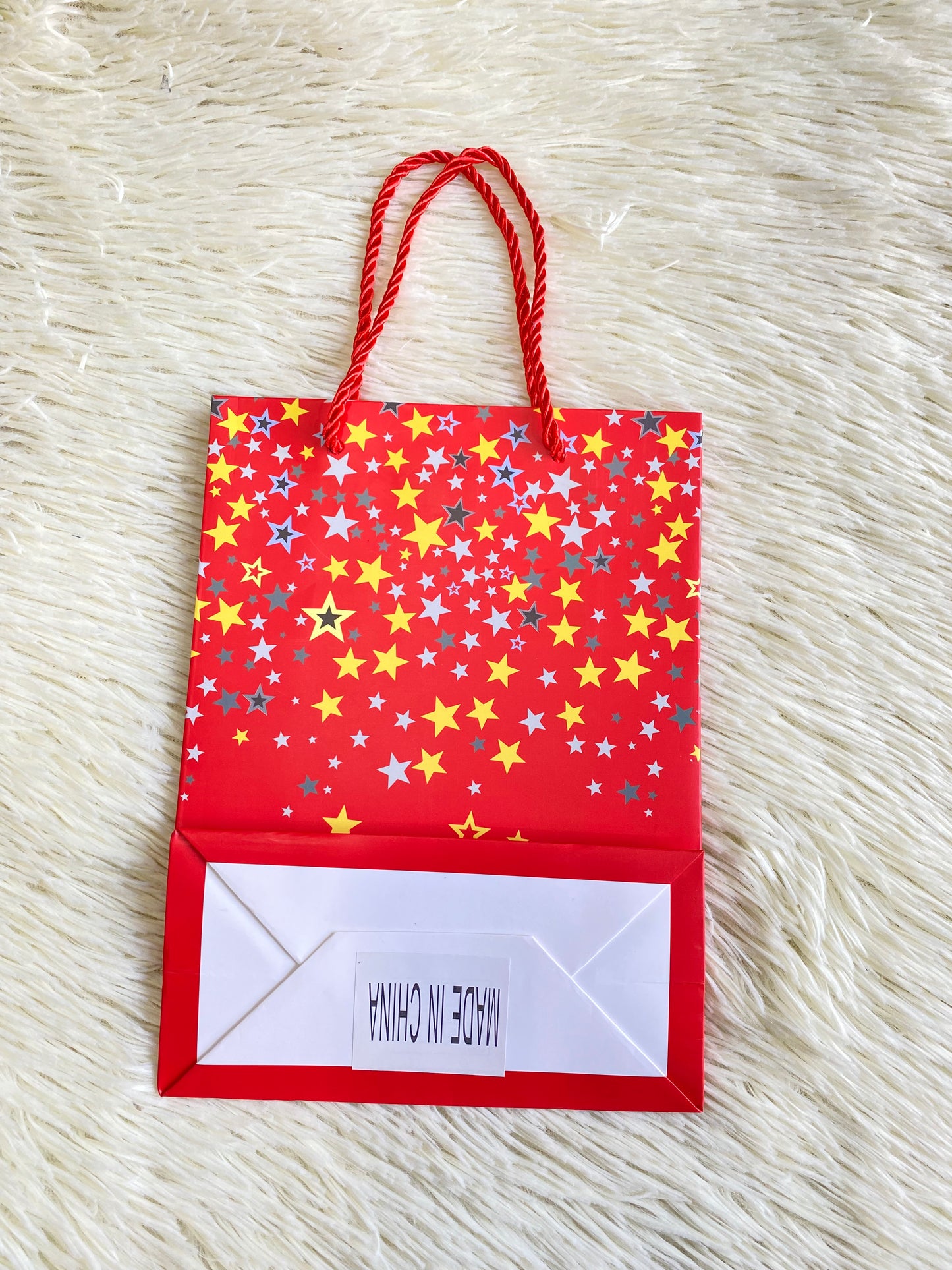 Shopping rojo con estrellas amarillas y azul con letras felicidades debajo. PEQUEÑO