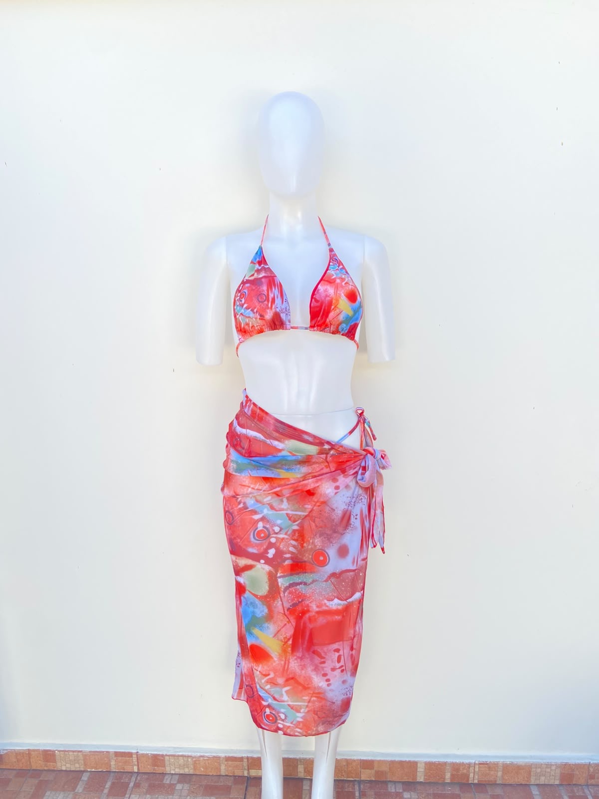 Biquini, de tres piezas con color rojo y coral combinados con detalles azules, verdes, amarillos, blancos y rosados.
