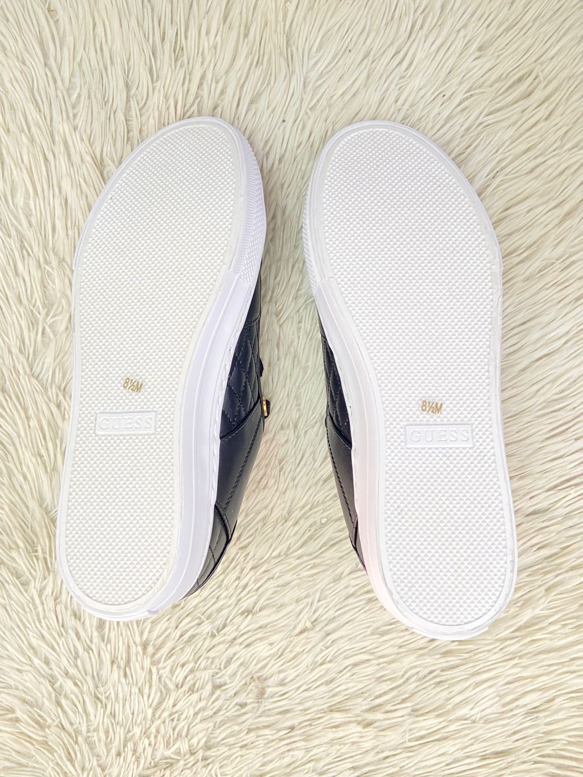 Tenis GUESS Original en color negro con detalles dorados y placa de la marca al lado en dorado.