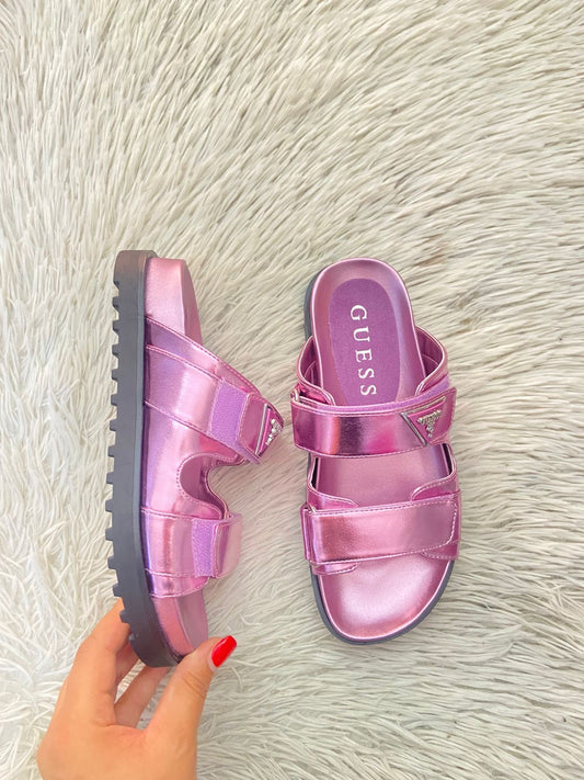 Sandalias GUESS Original, en color morado/lila metálico con dos tiras anchas ajustables al frente, placa de la marca en el lado y nombre de la marca en el interior con color plateado.