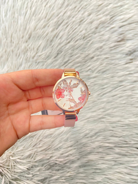 Reloj NINE WEST Original, con correa en color pastel, caja redonda en tono rose golden con diseño floral y nombre de la marca en el fondo al frente.