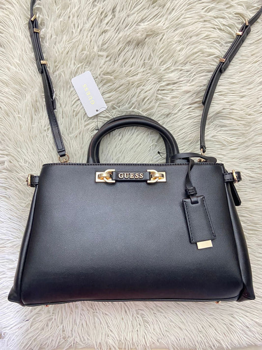 Cartera GUESS Original, color negra con placa de la marca al frente en color rosado y correa delgada adicional.