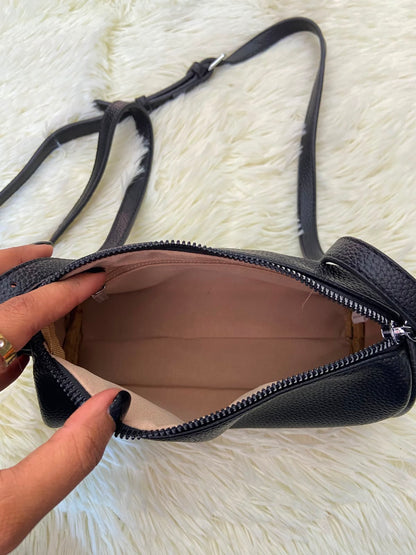Cartera, negra pequeña con lazo ajustable, en forma de cilindro.