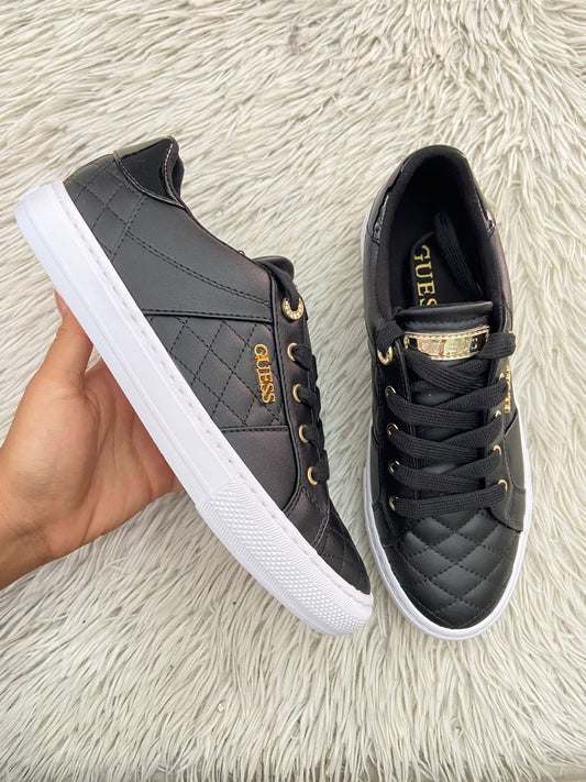 Tenis GUESS Original en color negro con detalles dorados y placa de la marca al lado en dorado.