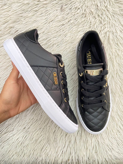 Tenis GUESS Original en color negro con detalles dorados y placa de la marca al lado en dorado.