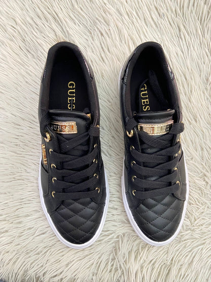 Tenis GUESS Original en color negro con detalles dorados y placa de la marca al lado en dorado.