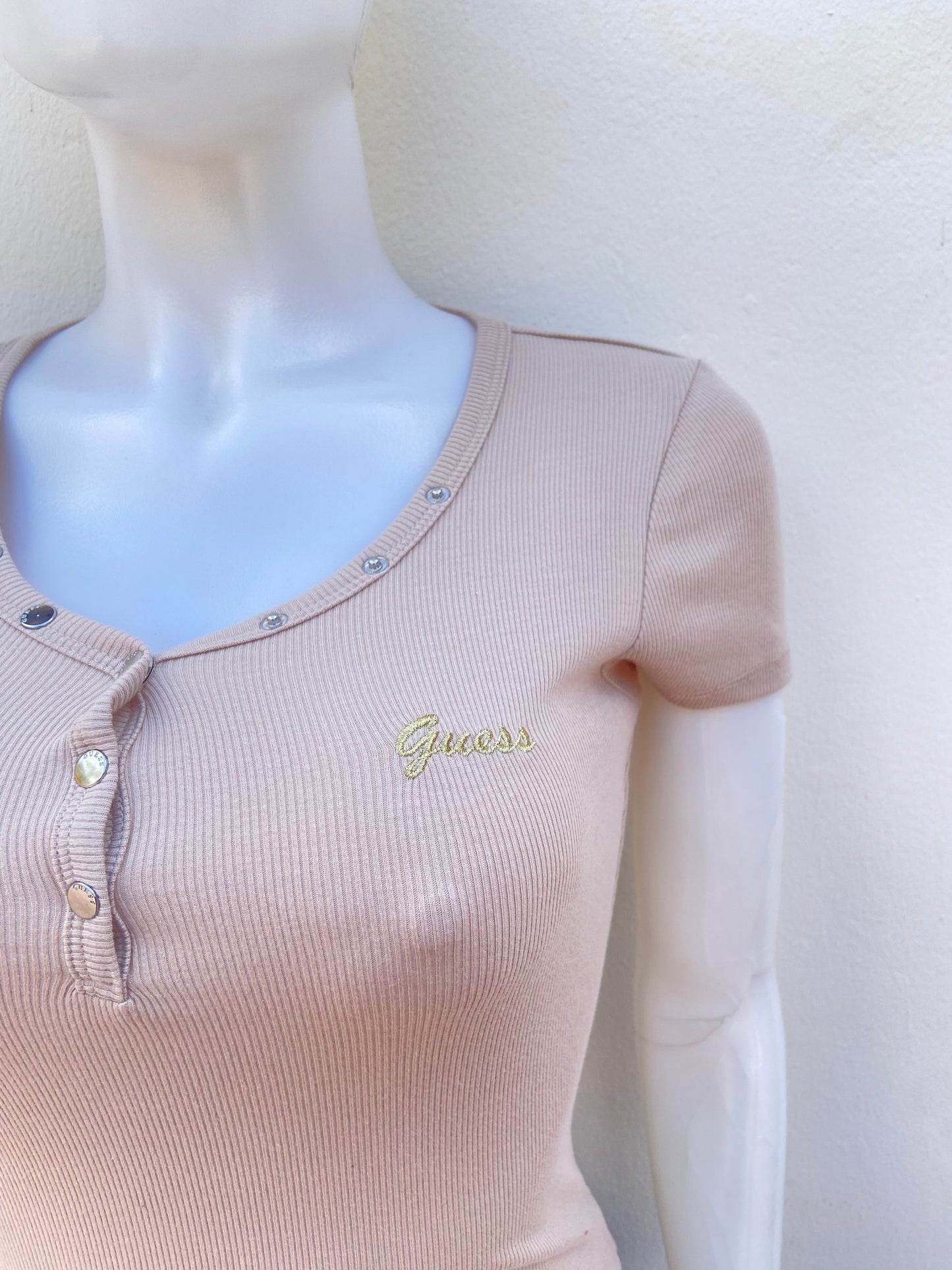 T-shirt GUESS original, crema ( beige ) con letras GUESS en cursivas en dorado y botones plateados.
