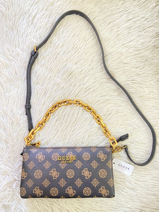 Cartera GUESS Original en color marron com estampado de la marca, cadena dorada y lazo adicional.