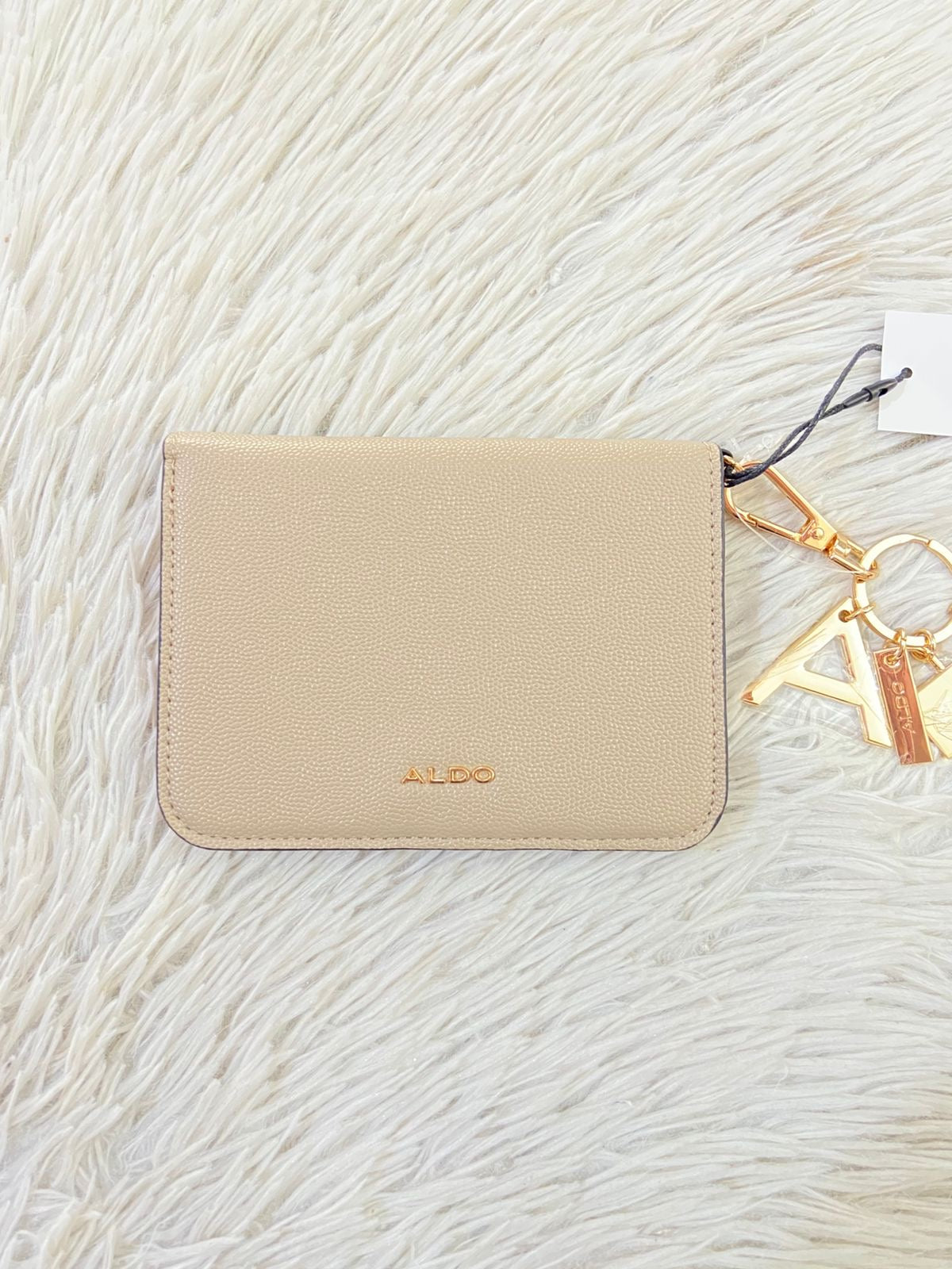 Monedero/ Cartera ALDO Original en color crema con placa de la marca al frente en color dorado y llavero adicional.