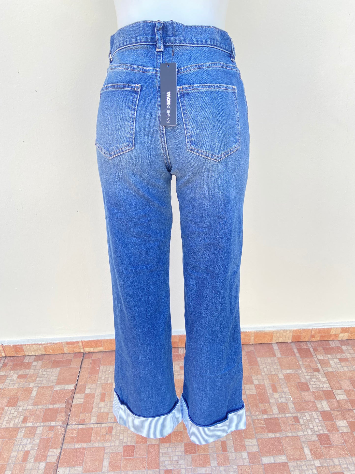 Pantalon Jean azul con tela azul con rayas blancas abajo, alto y con botón en color plateado.