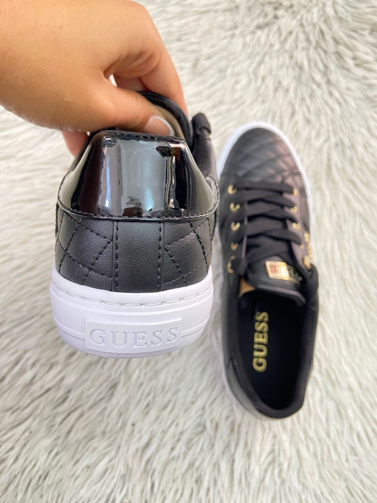 Tenis GUESS Original en color negro con detalles dorados y placa de la marca al lado en dorado.