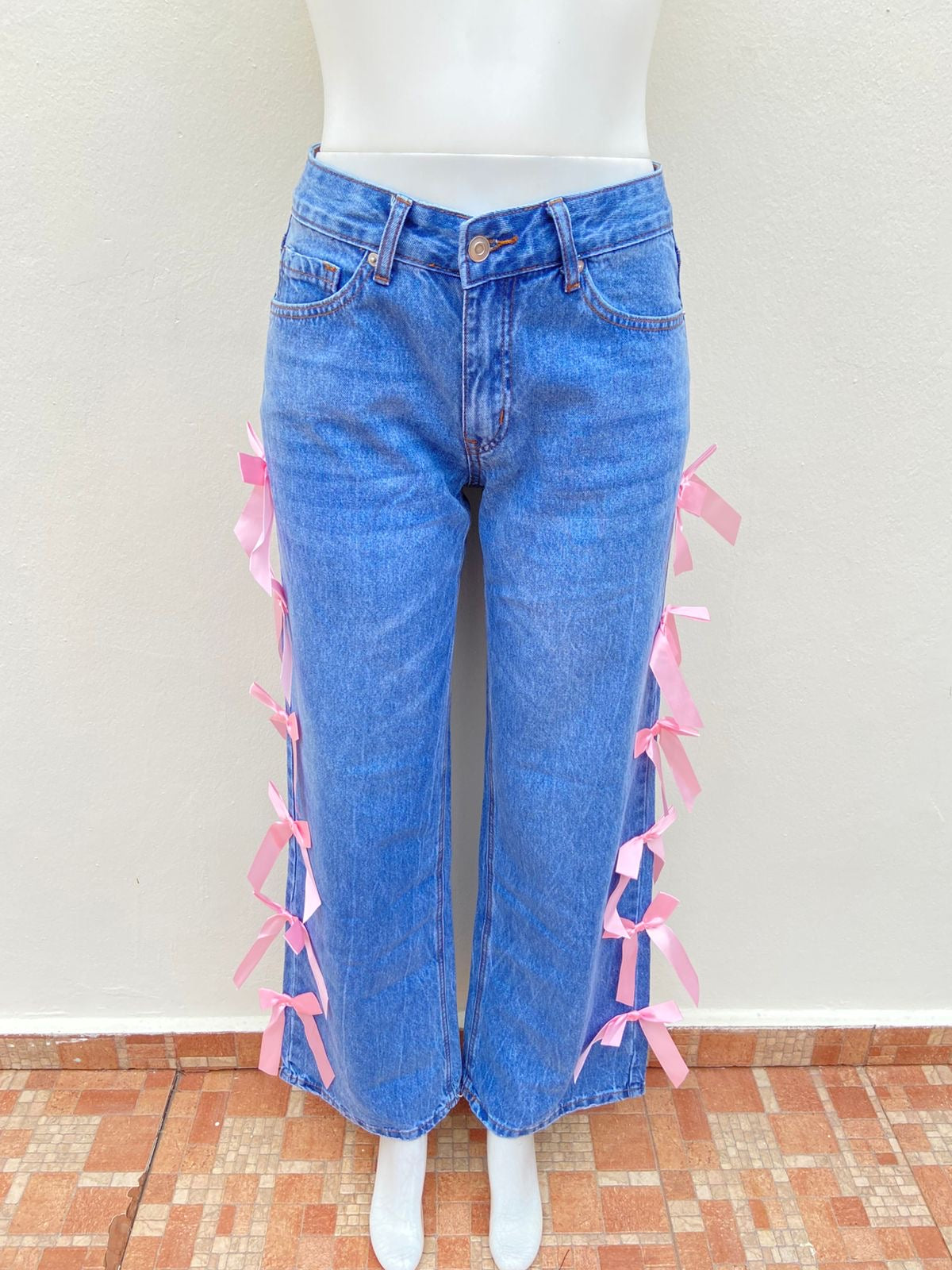 Pantalón Jean, azul liso con lazos en color rosado en los lados.