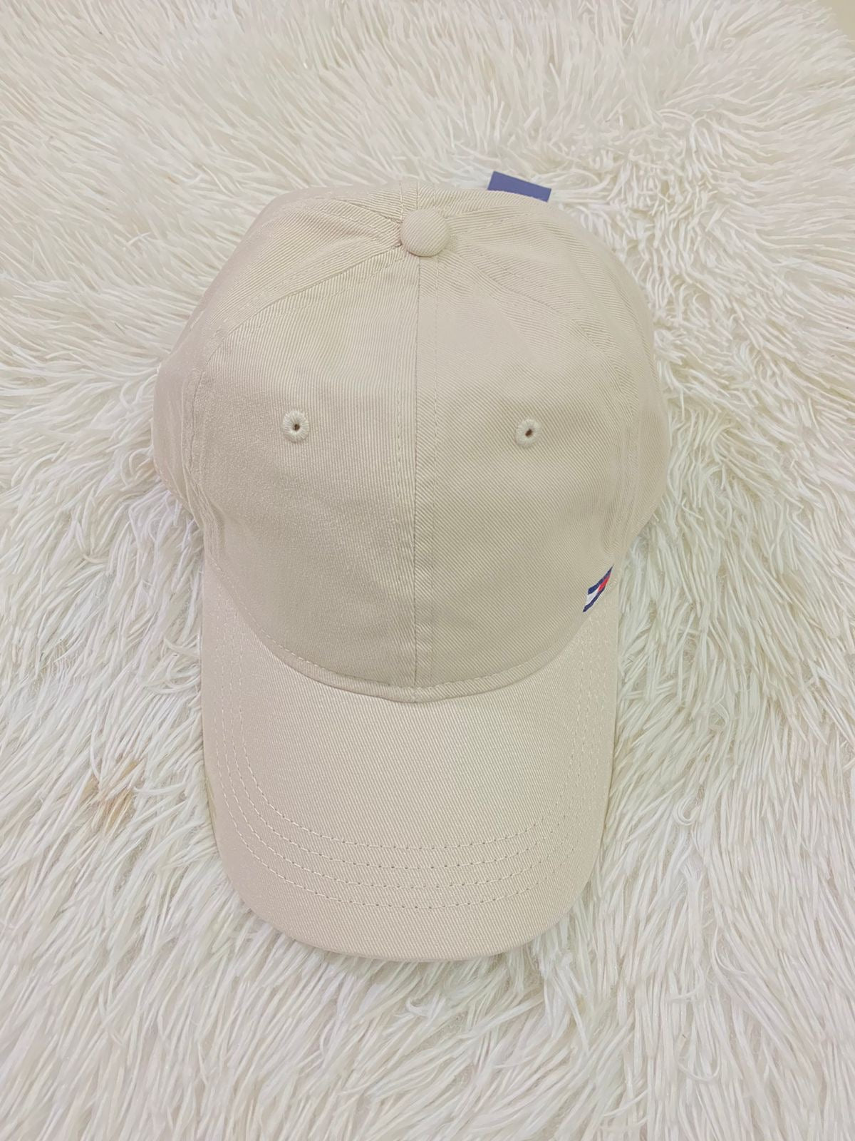 Gorra Tommy Hilfiger original crema con pequeño logotipo Tommy en la esquina y letras HILFIGER en azul.