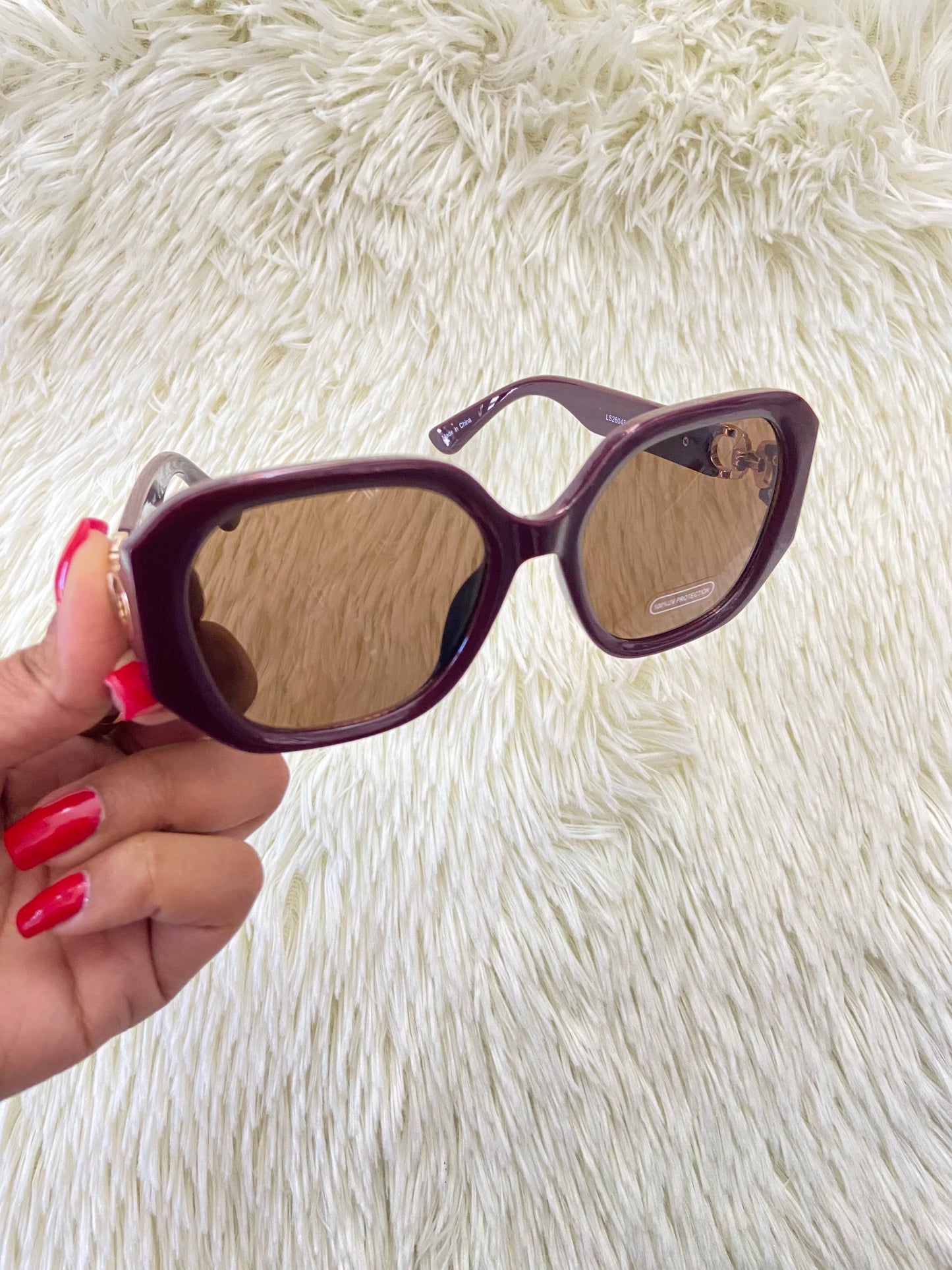 Lentes, rojo vino con micas oscuras y detalles dorado en los lados, con protección UV 100-400.
