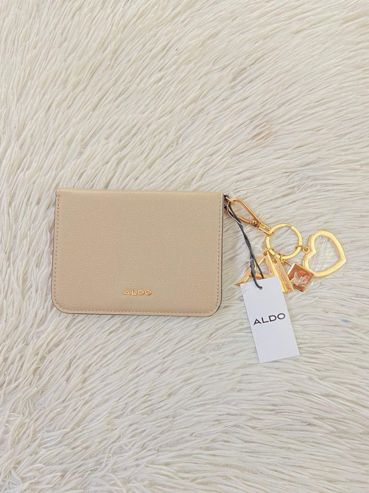 Monedero/ Cartera ALDO Original en color crema con placa de la marca al frente en color dorado y llavero adicional.