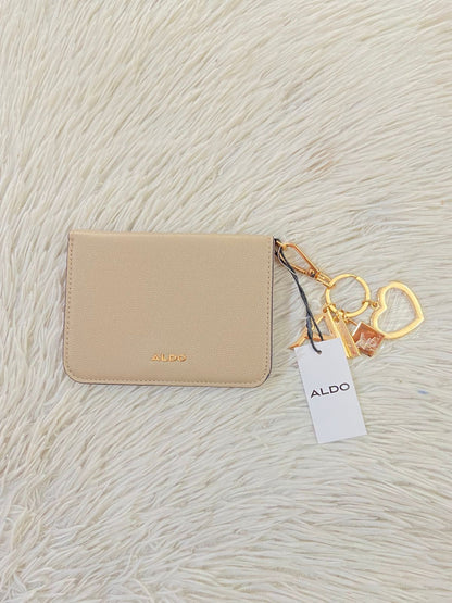 Monedero/ Cartera ALDO Original en color crema con placa de la marca al frente en color dorado y llavero adicional.