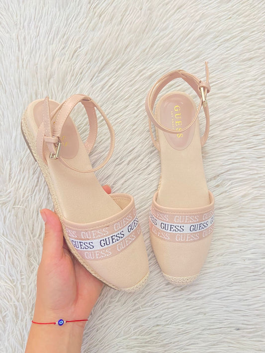 Sandalias GUESS Original en color rosado claro estilo alpargatas, banda con nombre repetido de la marca al frente y suela tipo plataforma baja.