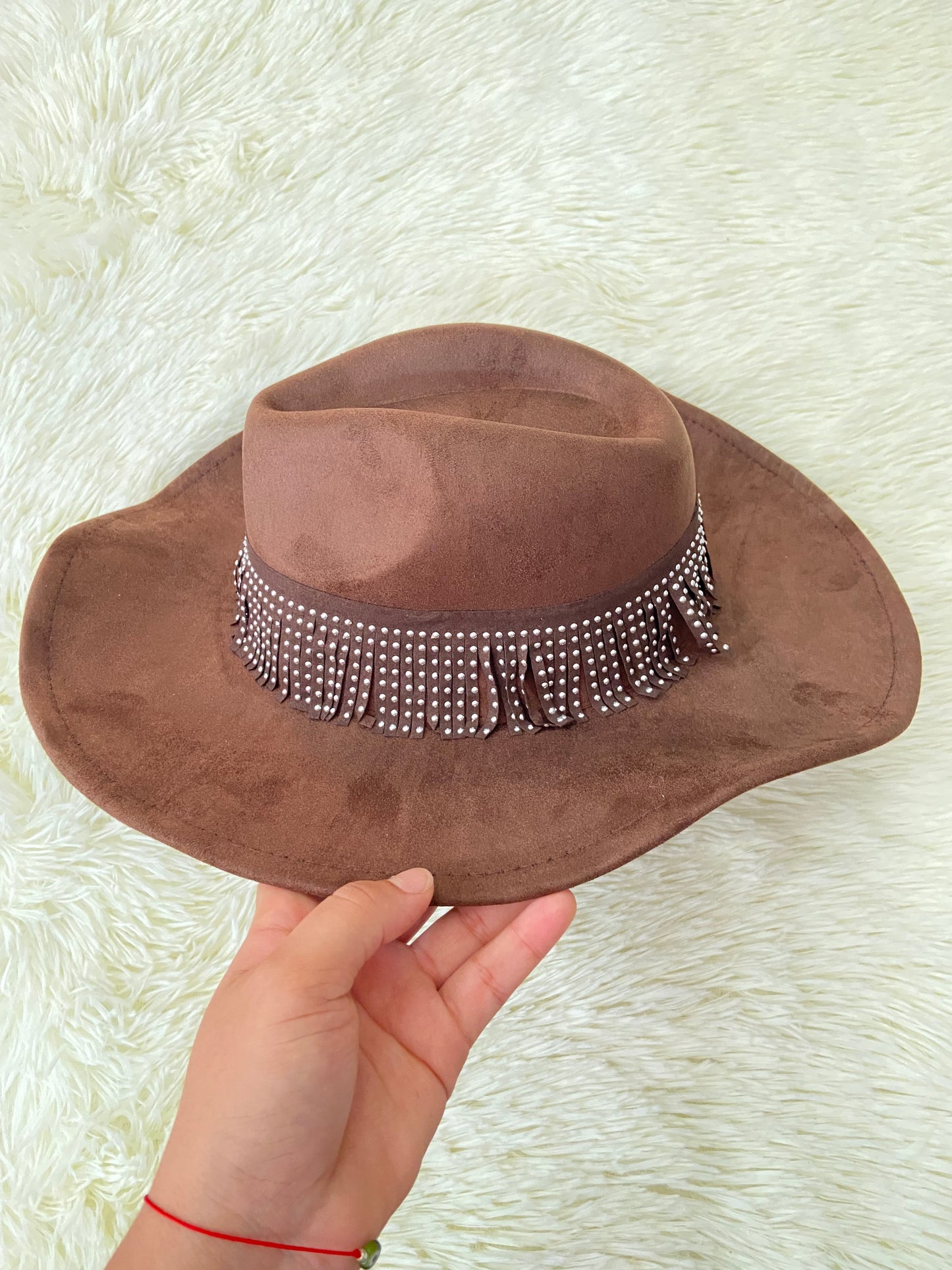 Sombrero marron con banda alrededor adornada con flecos y detalles metálicos.