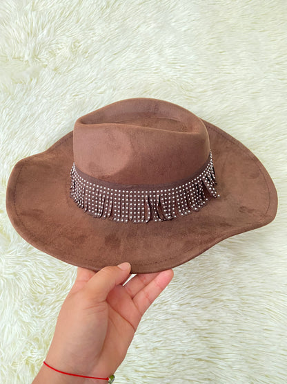 Sombrero marron con banda alrededor adornada con flecos y detalles metálicos.