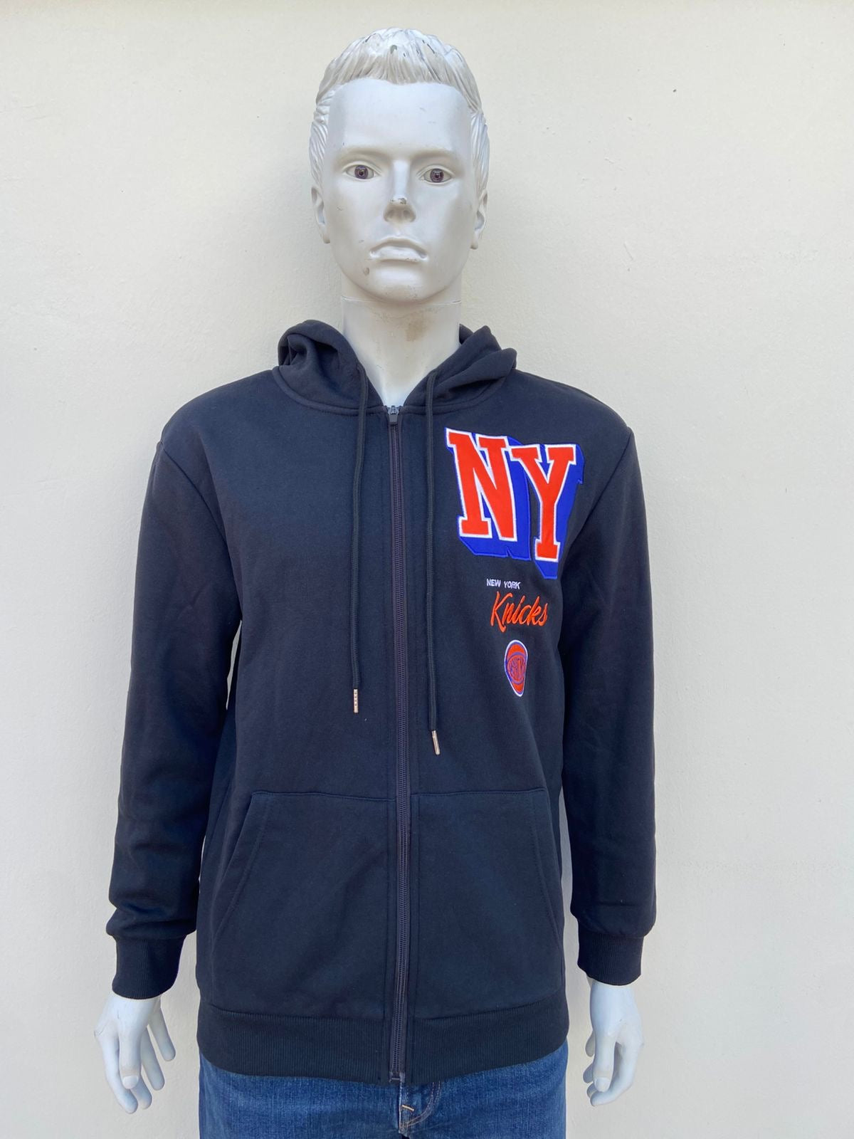 Abrigo NBA original NY KNICKS  negro con zipper y letras NY en color naranja al lado.
