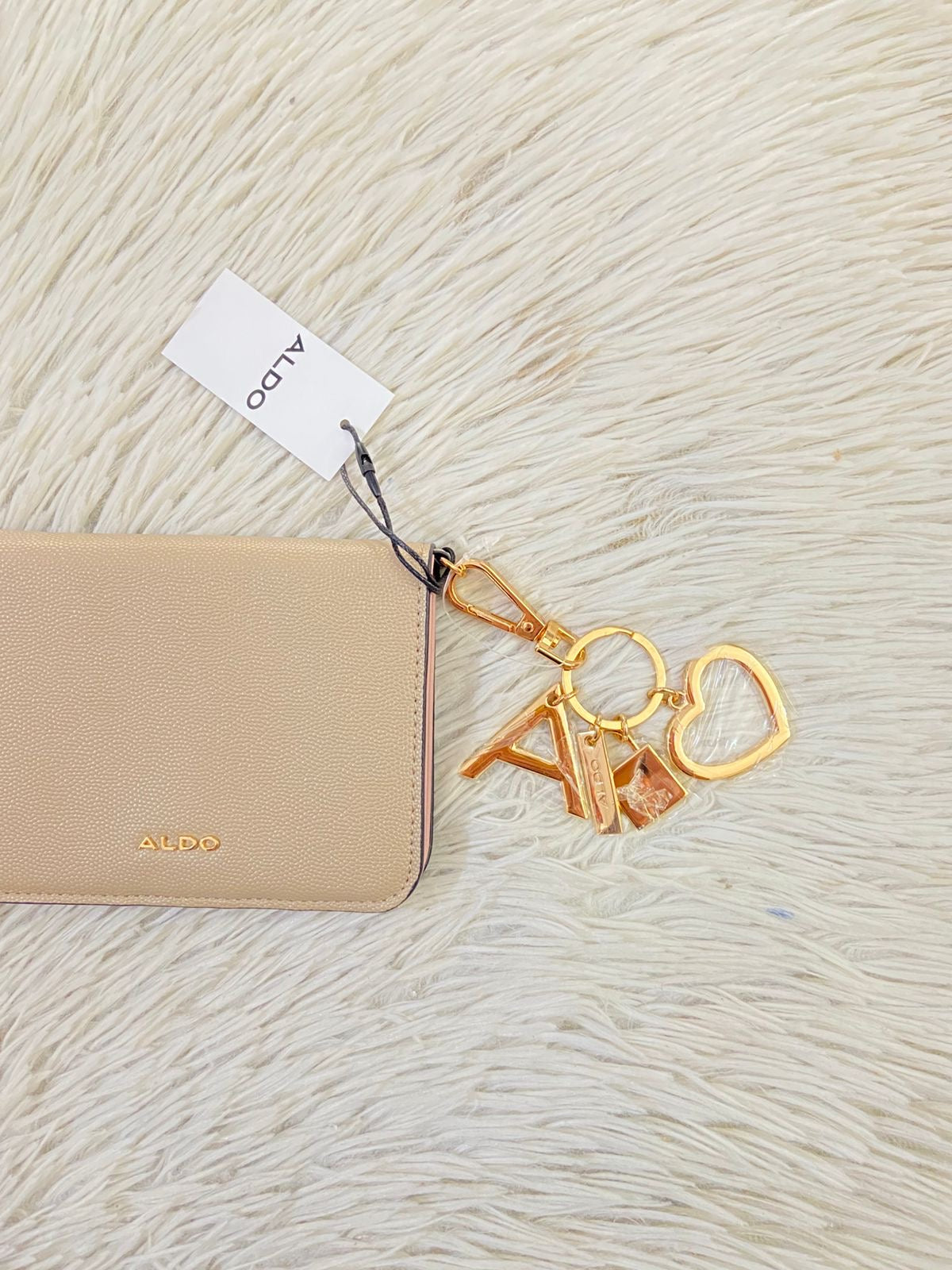 Monedero/ Cartera ALDO Original en color crema con placa de la marca al frente en color dorado y llavero adicional.