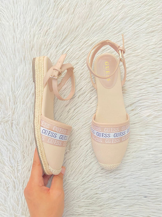Sandalias GUESS Original en color rosado claro estilo alpargatas, banda con nombre repetido de la marca al frente y suela tipo plataforma baja.