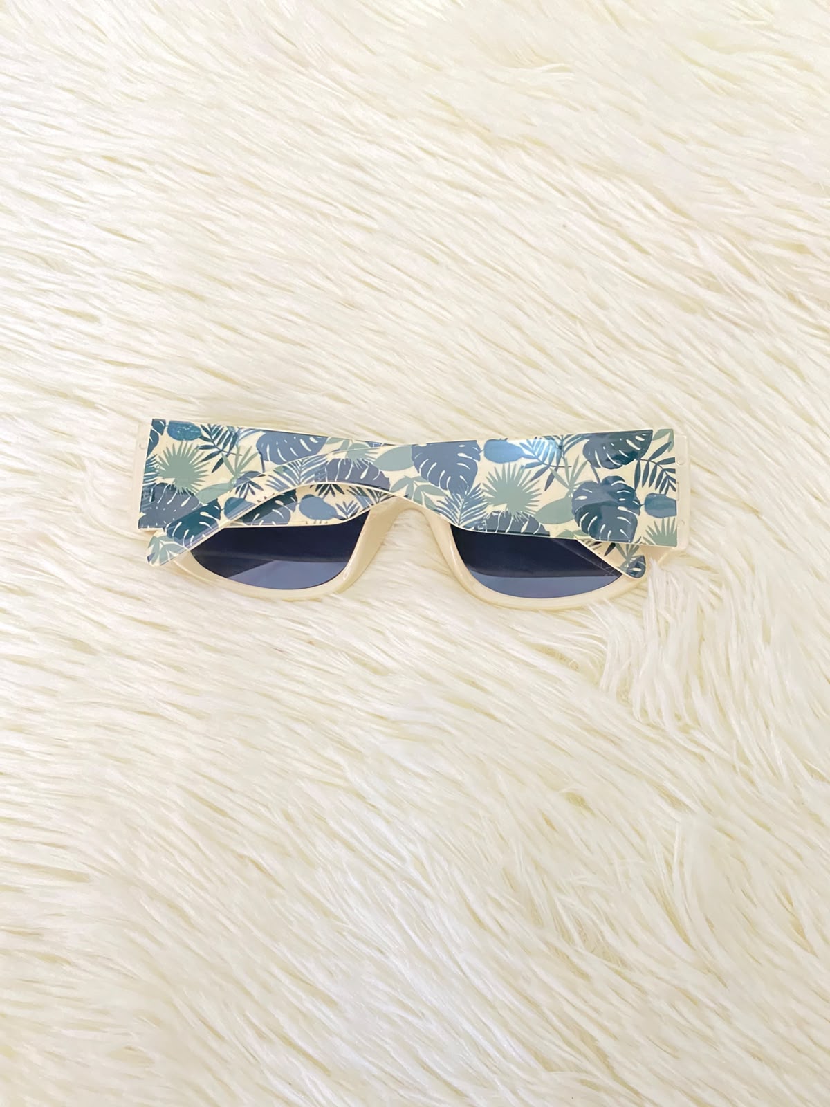 Lentes color crema con estampado de hojas tropicales en las patillas, estilo rectangular, con protección UV 100%.