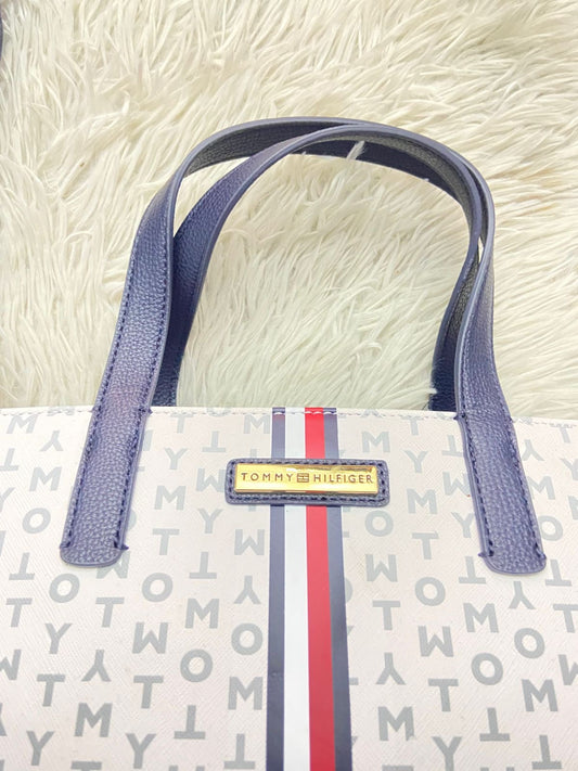 Cartera Tommy Hilfiger Original, blanco con estampado de la marca, línea al frente y correa adicional delgada.