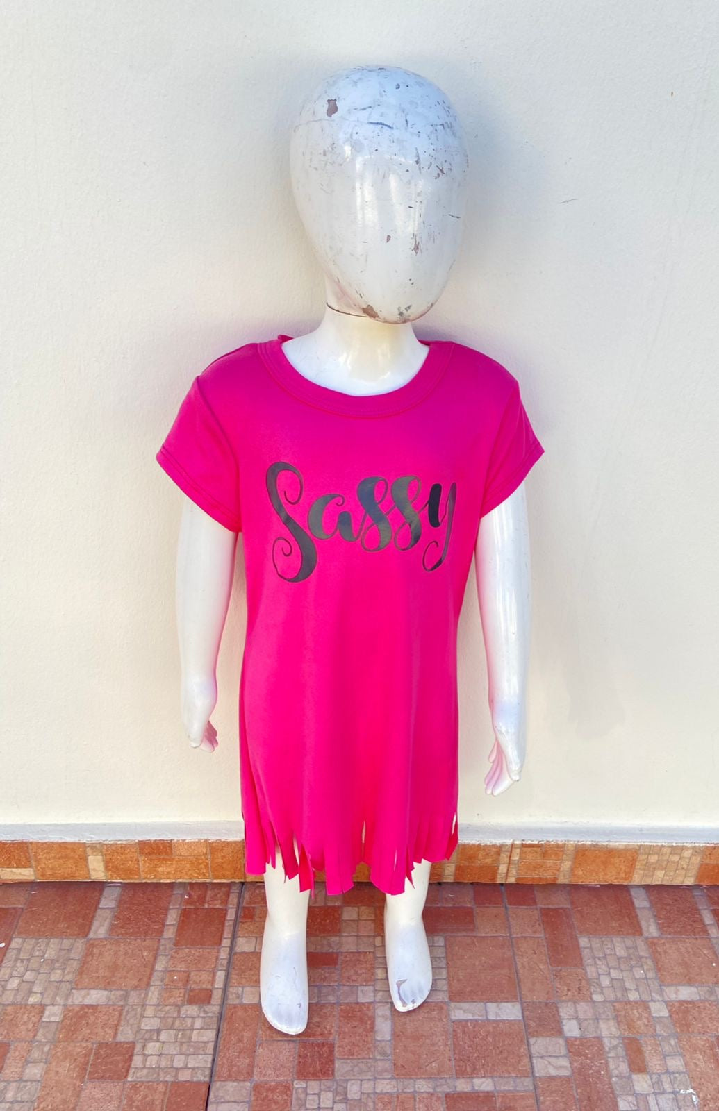 Vestido, rosado fucsia con letras SASSY ( atrevida )en negro y tiras en la parte inferior.