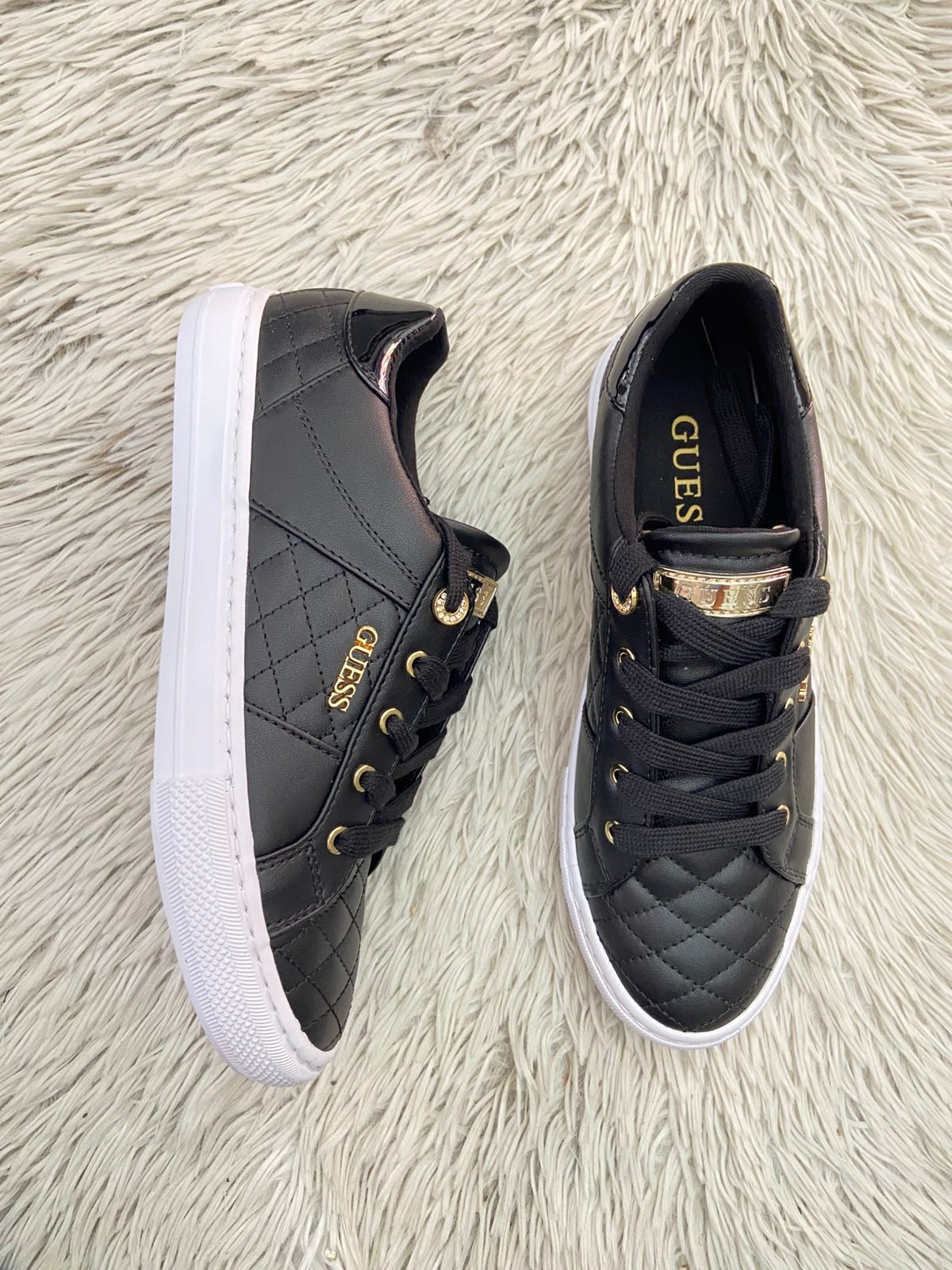 Tenis GUESS Original en color negro con detalles dorados y placa de la marca al lado en dorado.