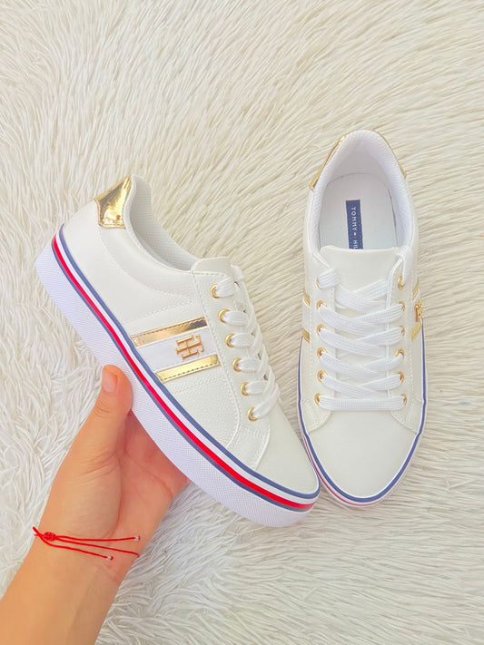 Tenis Tommy Hilfiger Original en color blanco con detalles dorados y linea abajo con color azul marino, blanco y rojo.  con letra de la marca atras Hilfiger