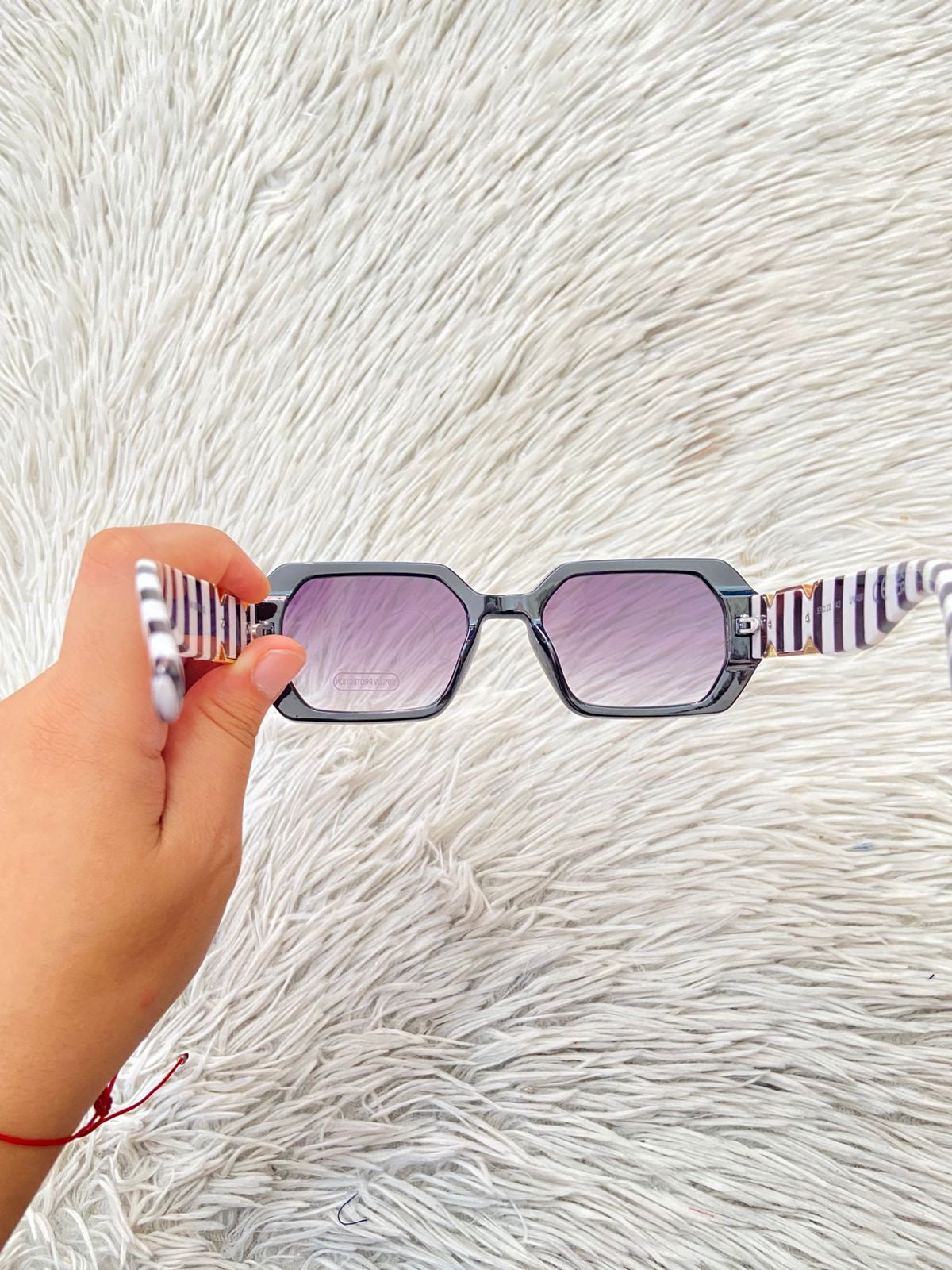 Lentes, negro con micas en color morado/ negro oscuro y montura con rayas blancas y negra y detalles en color dorado.