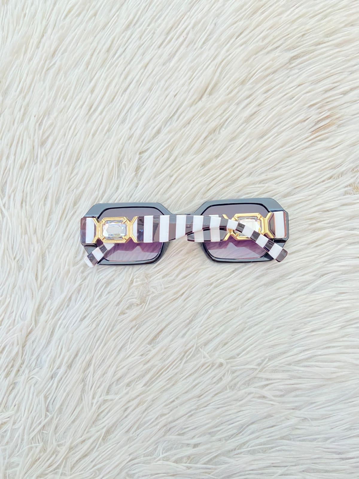 Lentes, negro con micas en color morado/ negro oscuro y montura con rayas blancas y negra y detalles en color dorado.