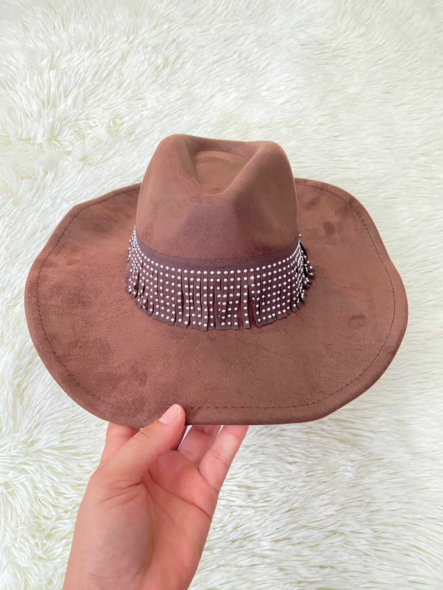 Sombrero marron con banda alrededor adornada con flecos y detalles metálicos.