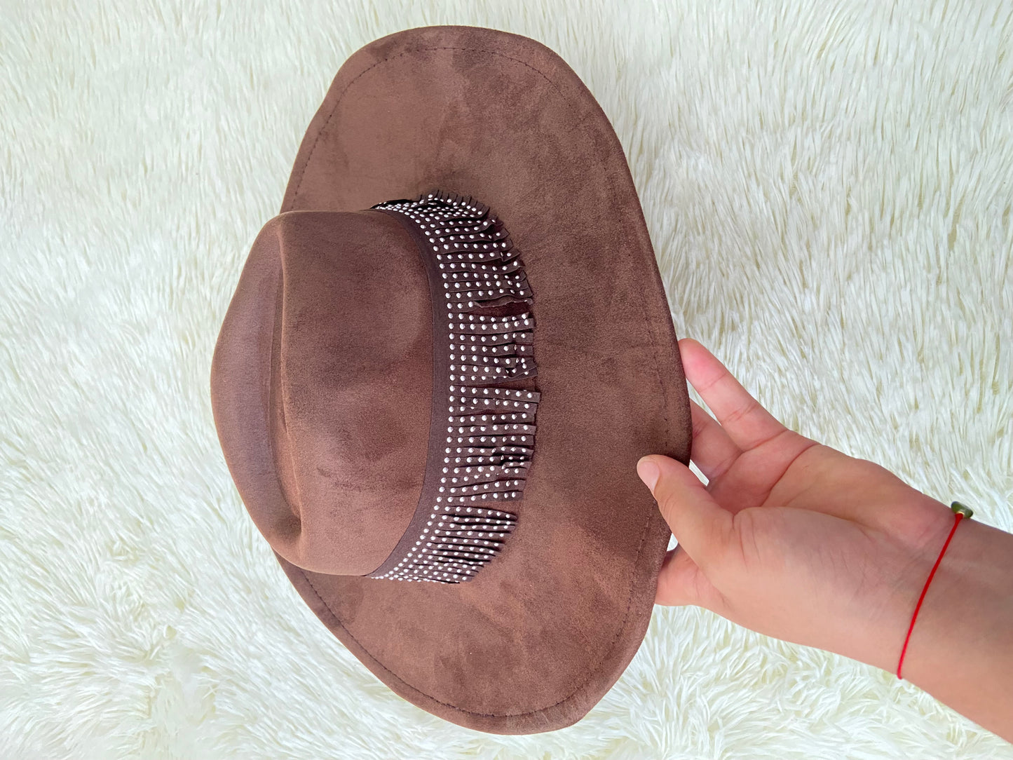Sombrero marron con banda alrededor adornada con flecos y detalles metálicos.