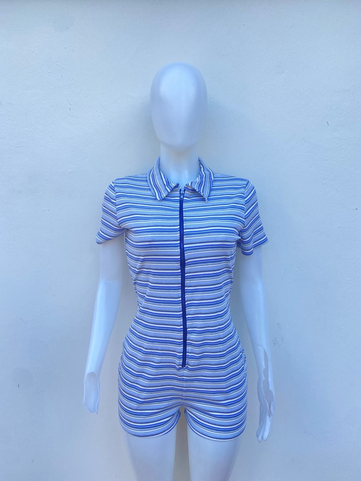Enterizo, blanco con estampado de lineas en tonos azules, corto con cuello y siper al frente.