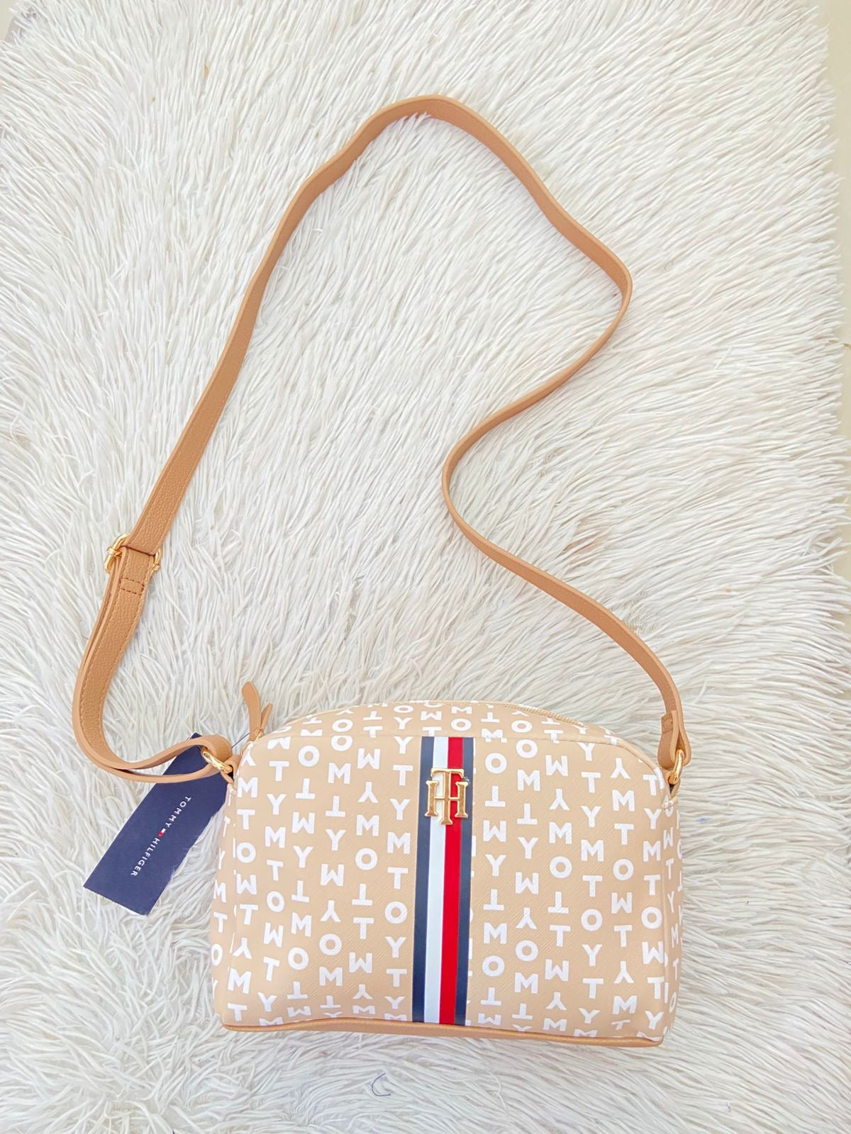 Cartera TOMMY HILFIGER original crema con estampado de letras TOMMY y banda de color rojo, azul y blanco y placa TH en dorado.
