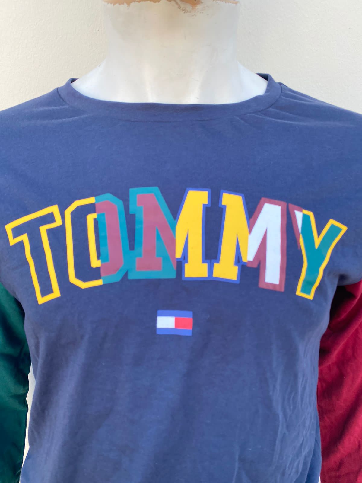 Suéter Tommy Hilfiger original azul marino con una manga en verde y otra en rojo, TOMMY en colores.