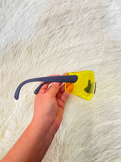 Lentes, sin montura con micas en color amarillo y patillas negras.