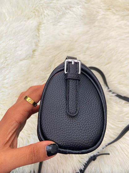 Cartera, negra pequeña con lazo ajustable, en forma de cilindro.