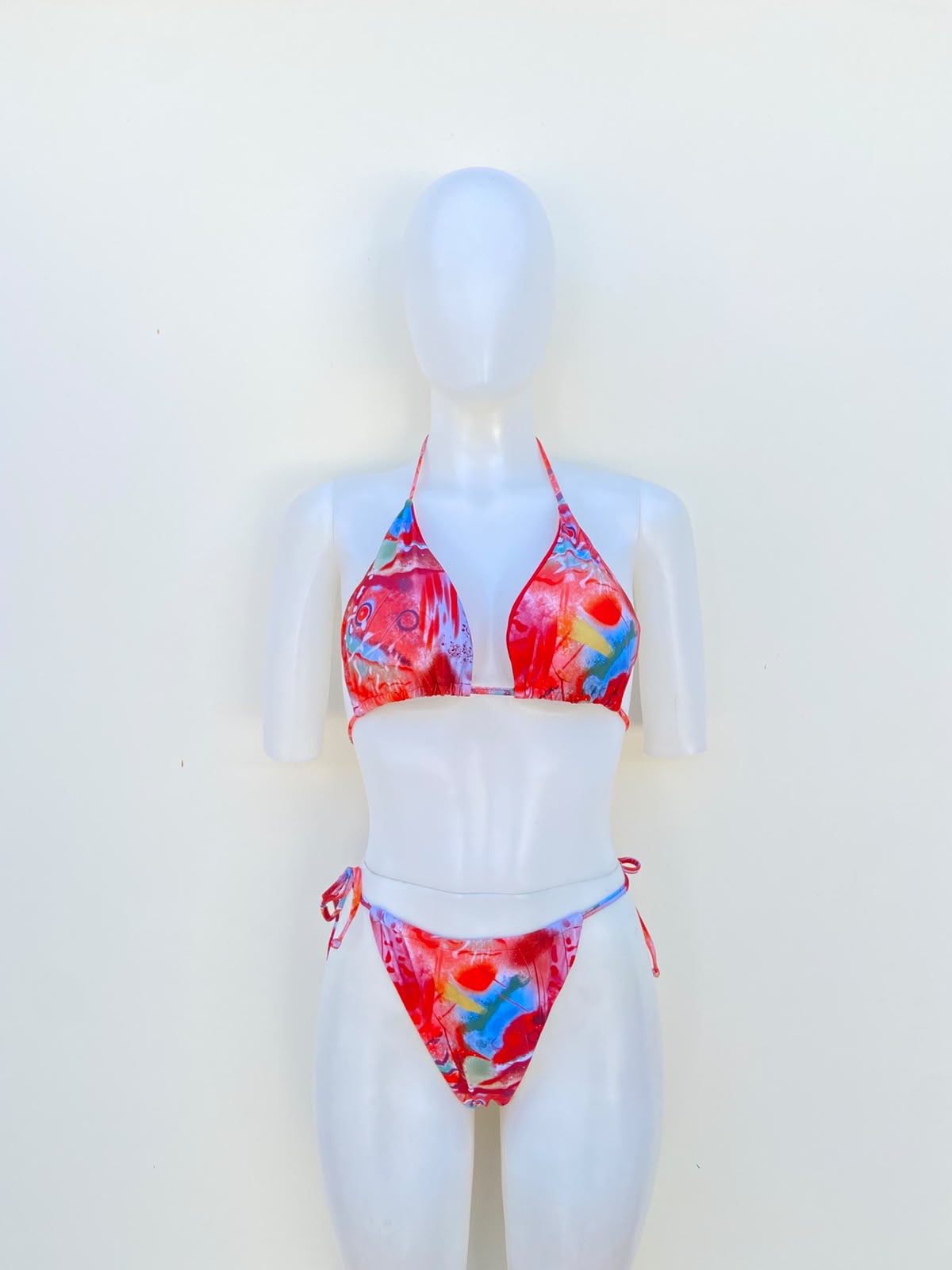 Biquini, de tres piezas con color rojo y coral combinados con detalles azules, verdes, amarillos, blancos y rosados.