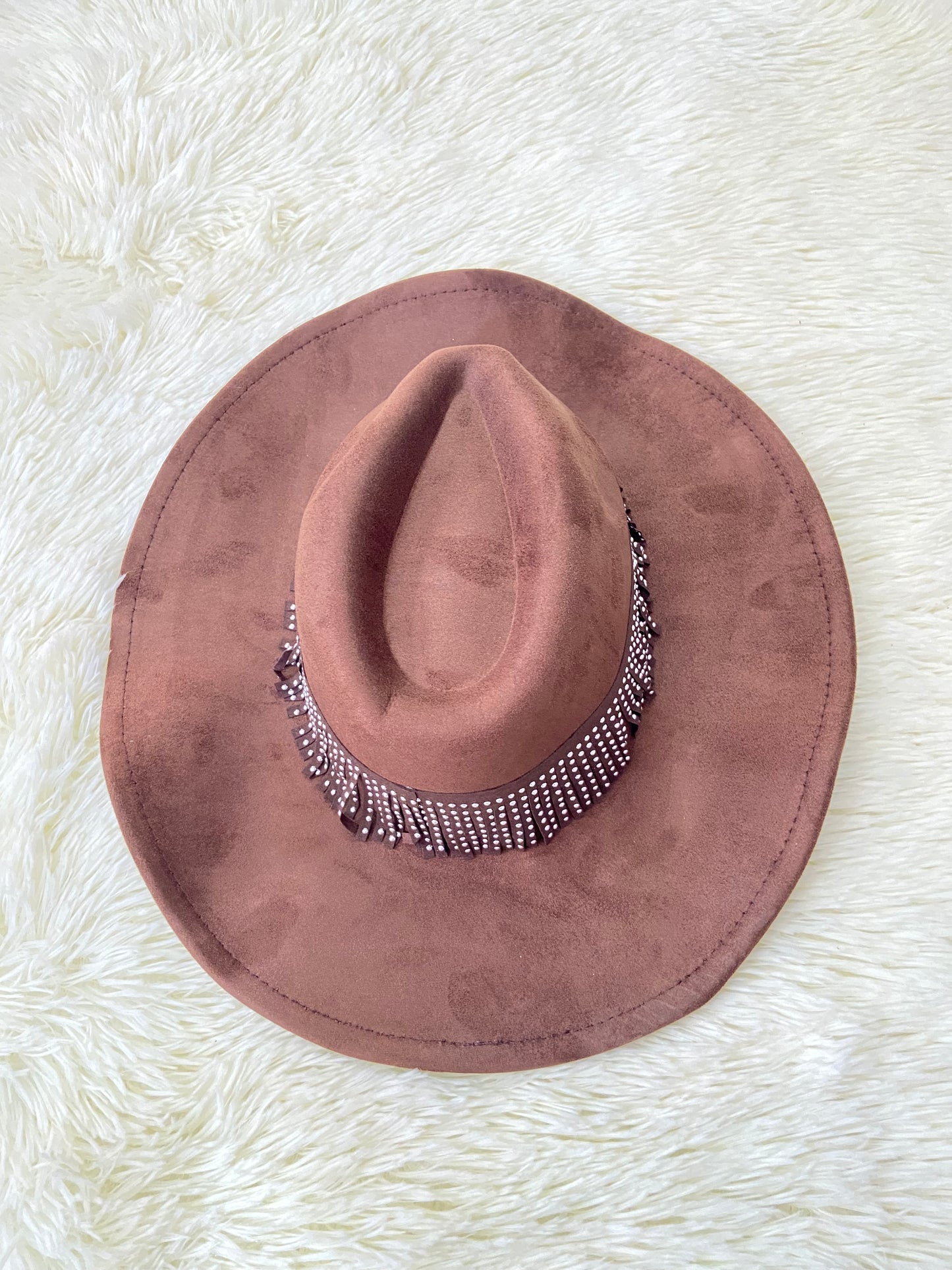 Sombrero marron con banda alrededor adornada con flecos y detalles metálicos.