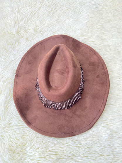 Sombrero marron con banda alrededor adornada con flecos y detalles metálicos.