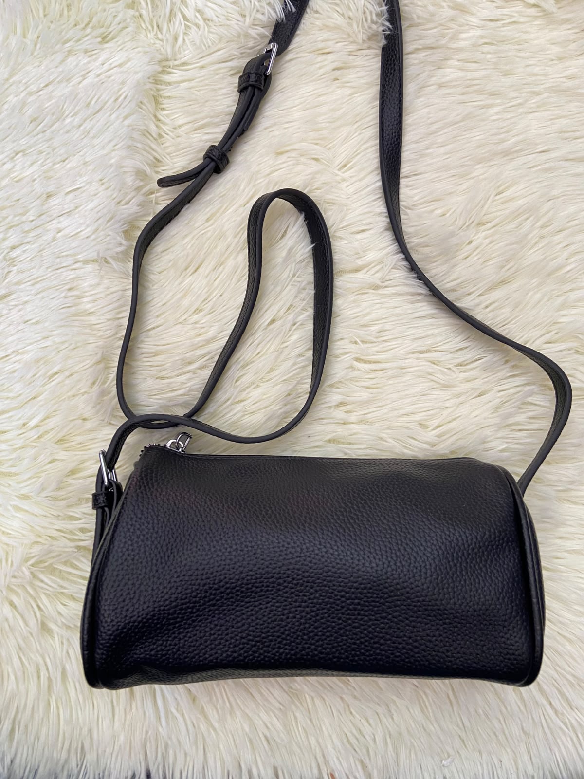 Cartera, negra pequeña con lazo ajustable, en forma de cilindro.
