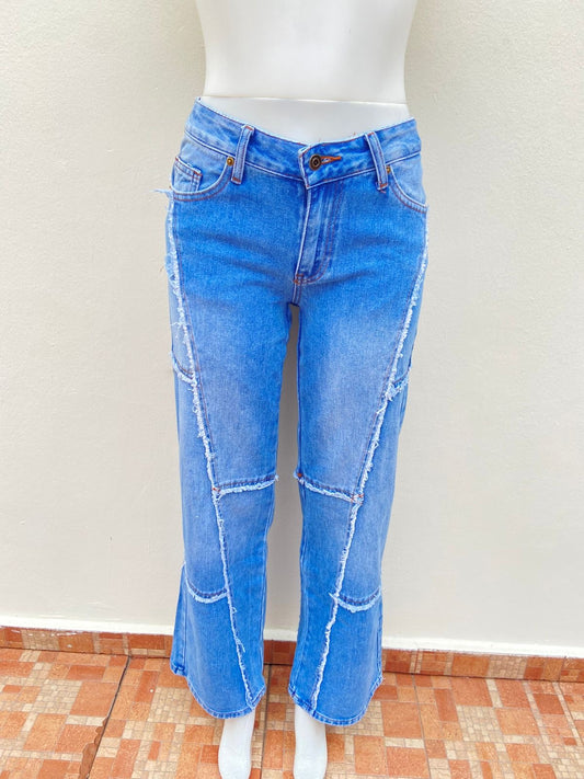 Pantalón Jean, azul claro con costura en hilo marrón y vuelos del Jean destruido en forma de líneas.