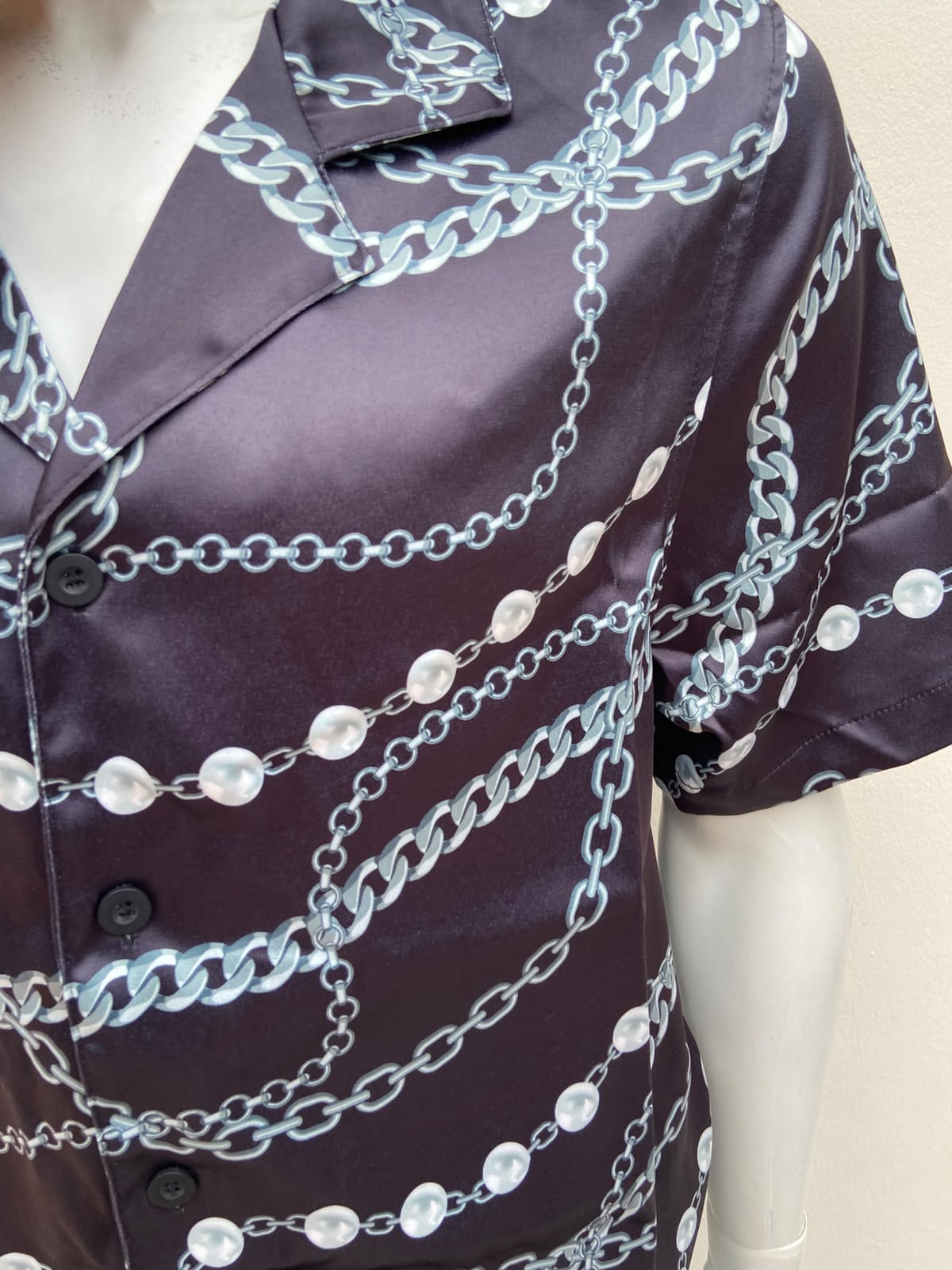 Camisa negra, con estampado de cadenas y perlas.