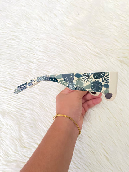 Lentes color crema con estampado de hojas tropicales en las patillas, estilo rectangular, con protección UV 100%.