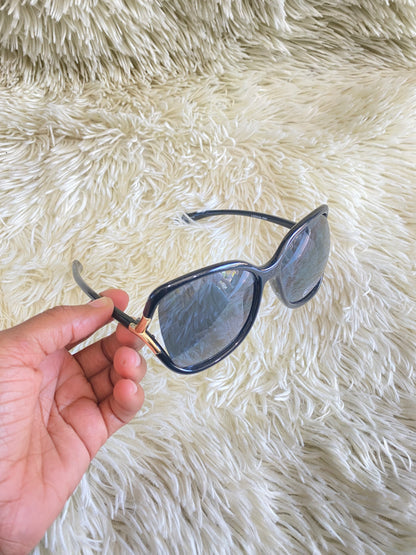 Lentes negro, ovalados, con detalle dorado en la esquina y micas claras PROTECCIÓN UV 100