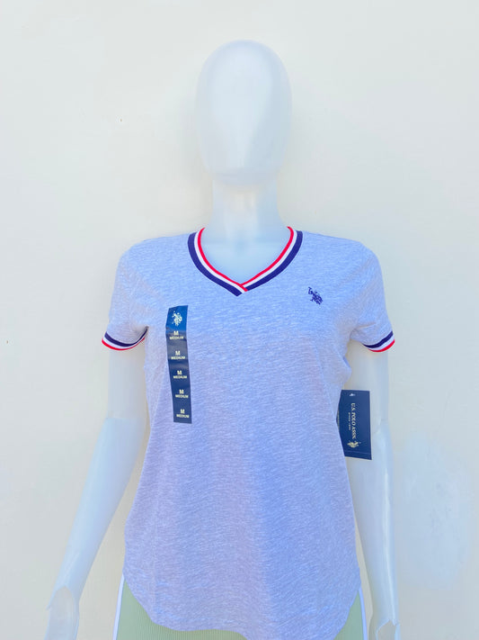 T-shirt U.S POLO ASSN. original en color gris con cuello V, logotipo de la marca al frente y banda en color azul marino, blanco y rojo en el cuello y mangas.