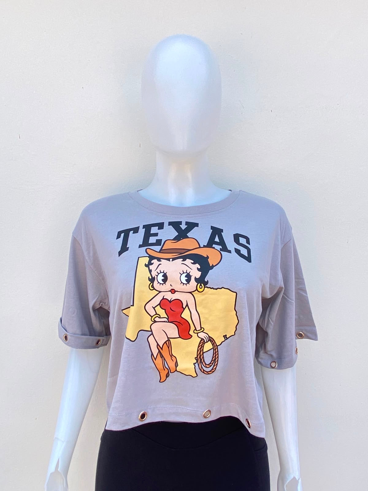 Top color gris con letra al frente TEXAS en color negro, la caricatura de Betty Boop con temática vaquera y detalles de ojales metálicos dorados.